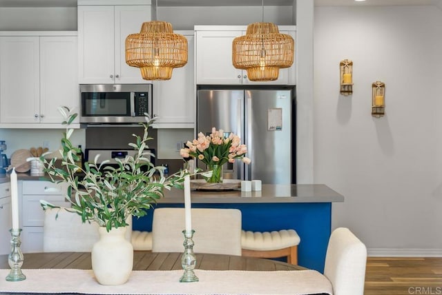 interior space with wood finished floors, baseboards, stainless steel appliances, white cabinets, and pendant lighting