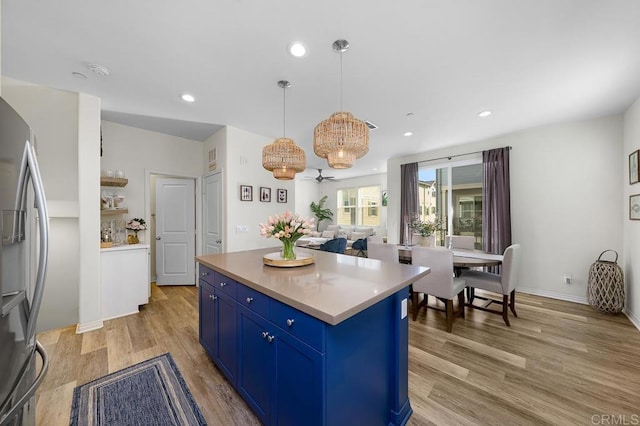 kitchen featuring light wood finished floors, blue cabinetry, a center island, light countertops, and freestanding refrigerator