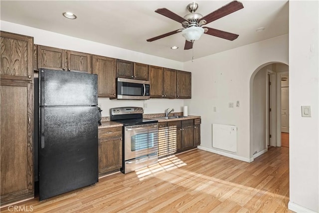 kitchen featuring arched walkways, ceiling fan, a sink, appliances with stainless steel finishes, and light wood-type flooring