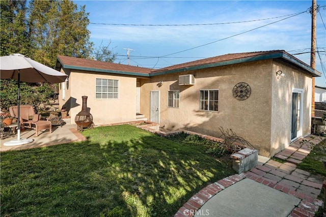 rear view of property featuring a patio area, stucco siding, a wall mounted air conditioner, and a yard