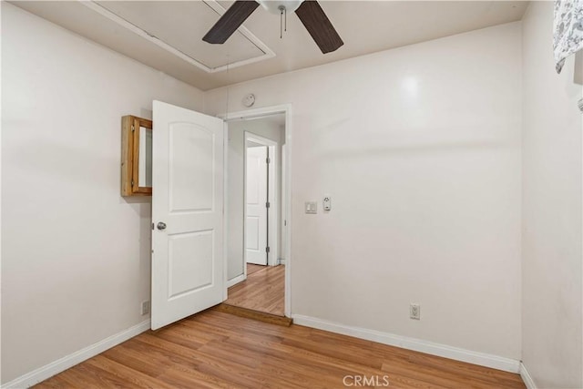 spare room featuring attic access, a ceiling fan, baseboards, and light wood finished floors