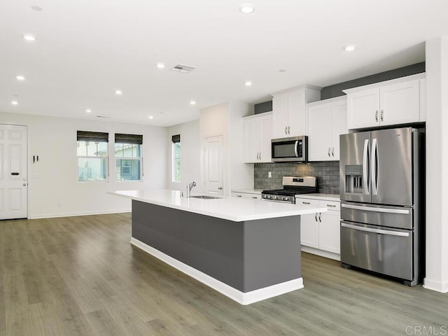 kitchen with visible vents, a center island with sink, a sink, tasteful backsplash, and stainless steel appliances