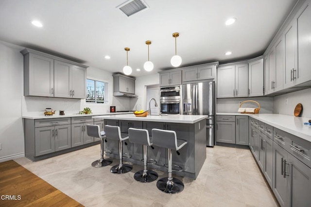 kitchen featuring a kitchen breakfast bar, visible vents, stainless steel appliances, and gray cabinetry