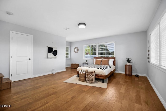 bedroom with multiple windows, wood finished floors, and baseboards