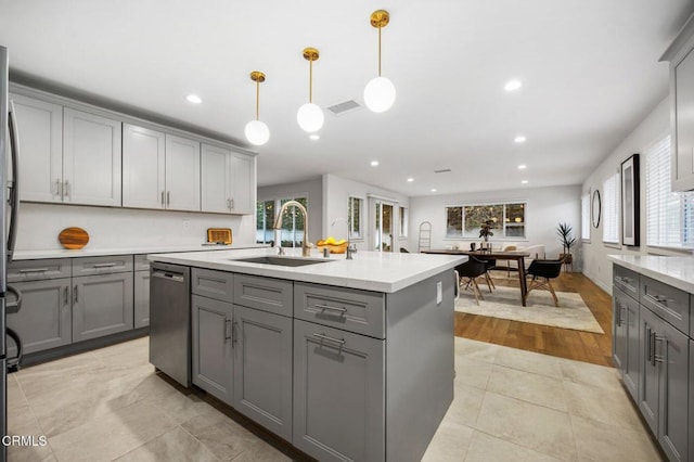 kitchen featuring visible vents, a sink, gray cabinetry, an island with sink, and stainless steel dishwasher