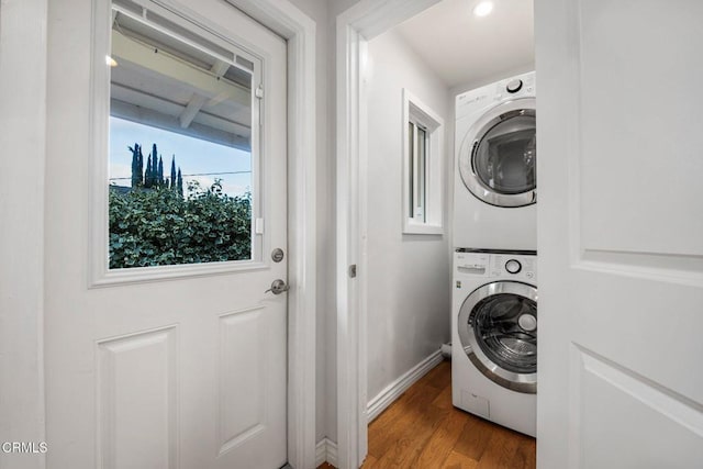 laundry area featuring laundry area, stacked washer / drying machine, baseboards, and wood finished floors