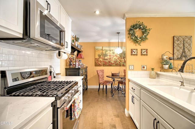 kitchen featuring a sink, decorative backsplash, ornamental molding, stainless steel appliances, and light wood-style floors