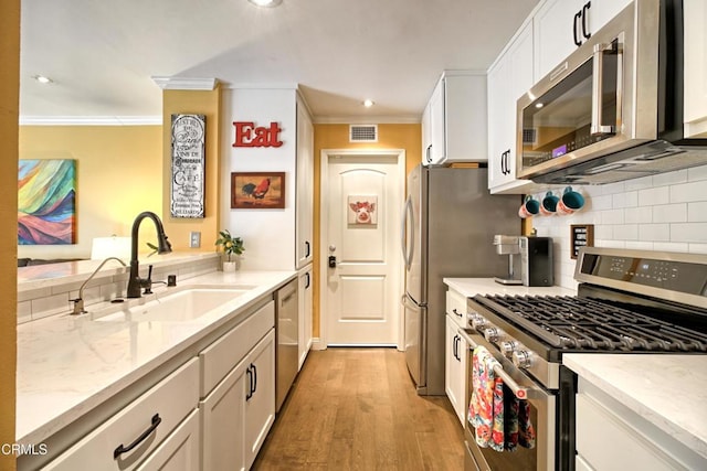 kitchen with visible vents, ornamental molding, stainless steel appliances, white cabinetry, and a sink