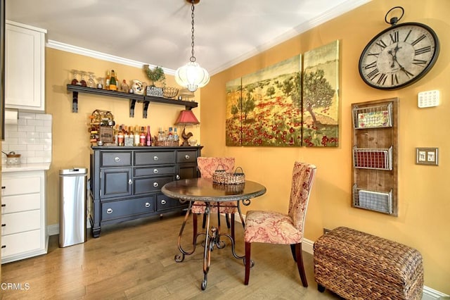 dining room featuring a bar, crown molding, wood finished floors, and baseboards