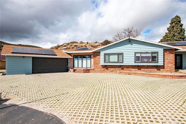 ranch-style home featuring brick siding, solar panels, driveway, and an attached garage