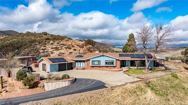 ranch-style home featuring roof mounted solar panels, curved driveway, fence, a garage, and brick siding