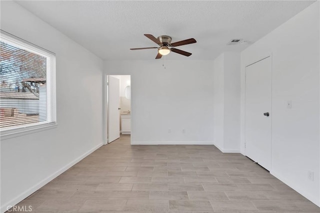 spare room featuring visible vents, baseboards, a textured ceiling, and ceiling fan