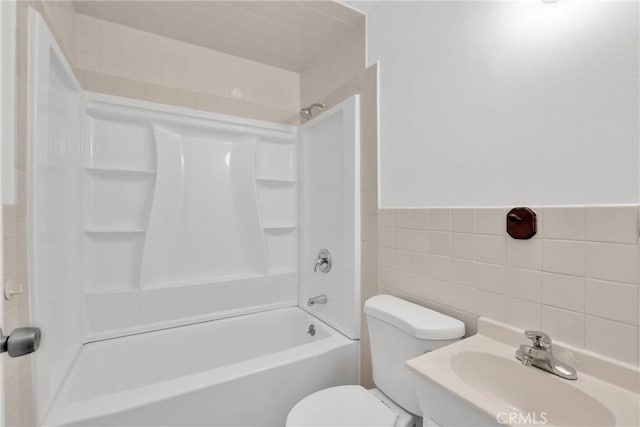 bathroom featuring a wainscoted wall, toilet, bathing tub / shower combination, tile walls, and a sink