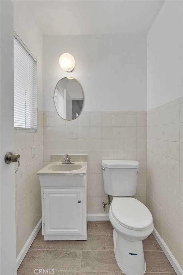 bathroom featuring vanity, wood finished floors, a wainscoted wall, tile walls, and toilet