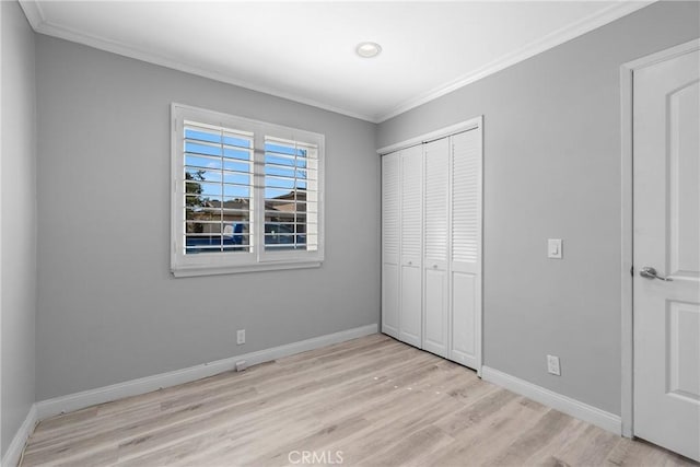 unfurnished bedroom with a closet, baseboards, ornamental molding, and light wood-style flooring