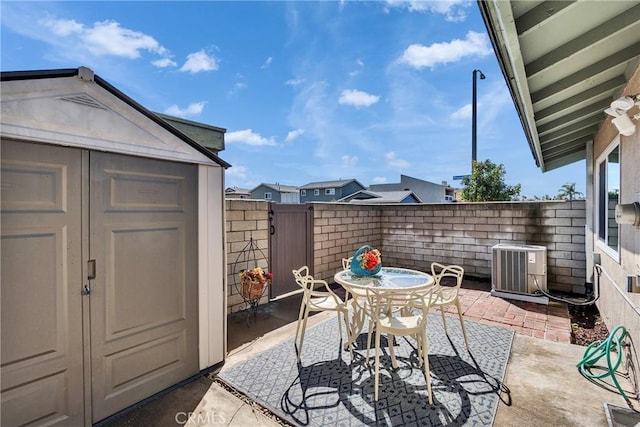 view of patio with a fenced backyard, a storage shed, an outdoor structure, outdoor dining area, and central AC unit