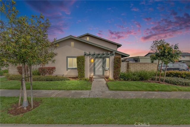 view of front of home featuring stucco siding, a front yard, and fence