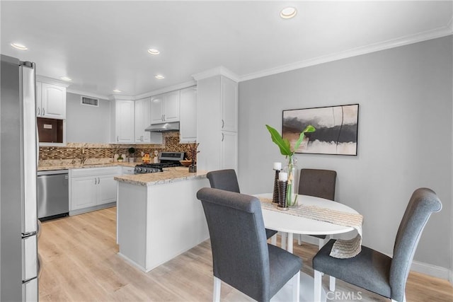 kitchen with visible vents, under cabinet range hood, white cabinetry, stainless steel appliances, and decorative backsplash