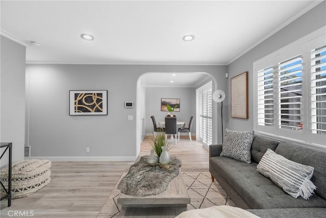 living room featuring ornamental molding, baseboards, arched walkways, and light wood-type flooring