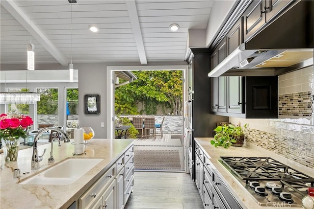 kitchen with backsplash, under cabinet range hood, beamed ceiling, stainless steel gas cooktop, and a sink