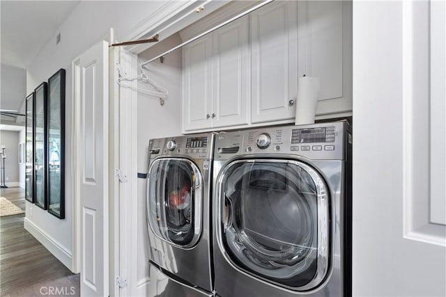 clothes washing area featuring wood finished floors, cabinet space, washing machine and dryer, and baseboards