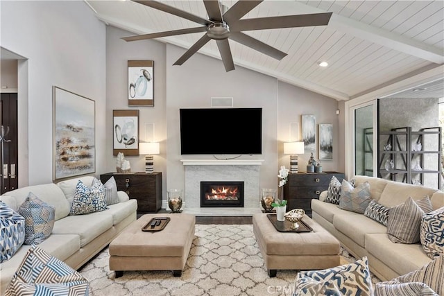 living area with a ceiling fan, a lit fireplace, and vaulted ceiling with beams