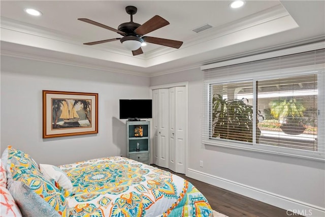 bedroom featuring visible vents, baseboards, dark wood finished floors, a tray ceiling, and ornamental molding