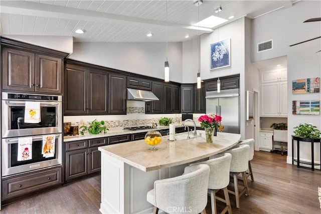 kitchen featuring visible vents, a breakfast bar, under cabinet range hood, dark wood finished floors, and stainless steel appliances