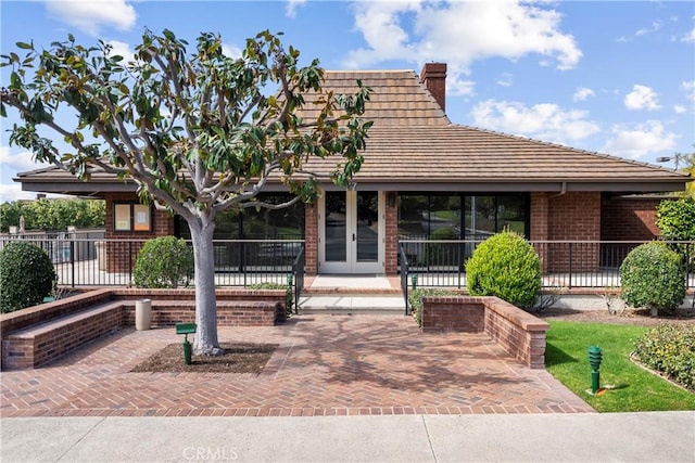 view of front of property featuring fence, a chimney, french doors, a tiled roof, and brick siding