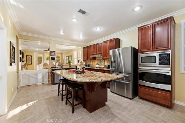 kitchen featuring visible vents, under cabinet range hood, light stone counters, a kitchen breakfast bar, and stainless steel appliances