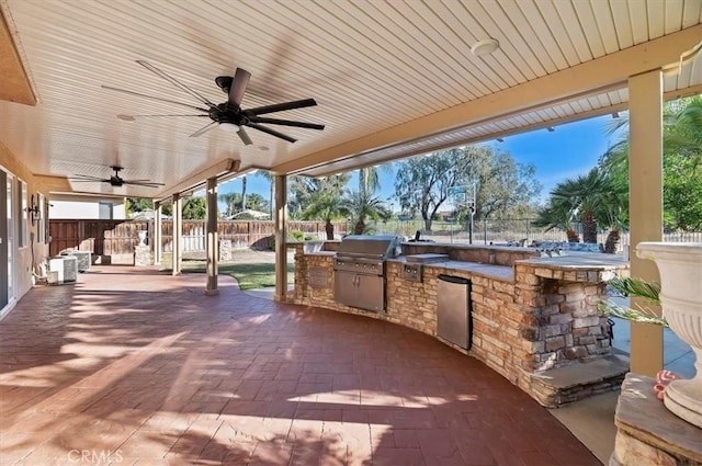 view of patio / terrace with grilling area, an outdoor kitchen, a ceiling fan, and a fenced backyard