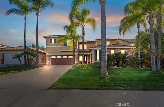 mediterranean / spanish home featuring stucco siding, stone siding, roof mounted solar panels, a yard, and concrete driveway