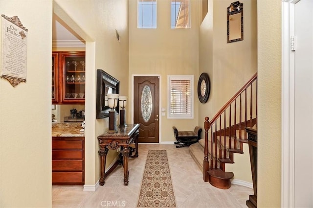 foyer entrance featuring visible vents, crown molding, baseboards, a towering ceiling, and stairs