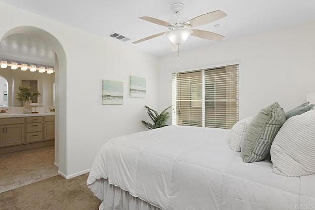 bedroom with visible vents, connected bathroom, baseboards, light carpet, and arched walkways