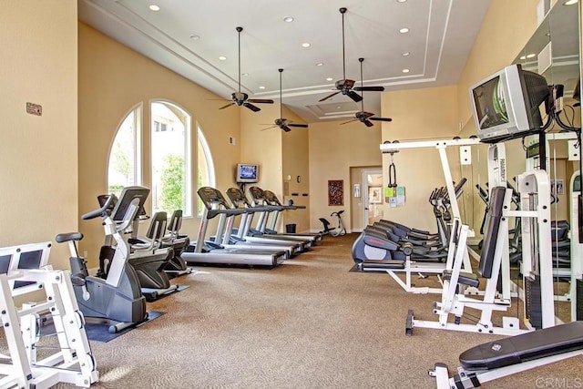 gym with a raised ceiling, a high ceiling, recessed lighting, and a ceiling fan