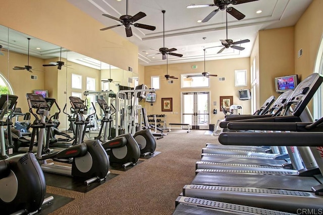 exercise room with visible vents, attic access, a tray ceiling, a towering ceiling, and a ceiling fan