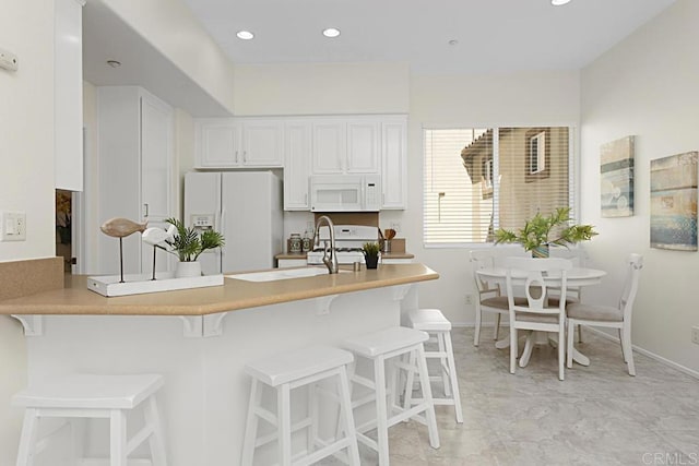 kitchen with a breakfast bar, white cabinetry, white appliances, a peninsula, and light countertops