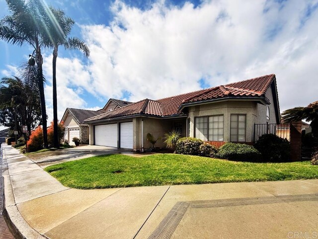 mediterranean / spanish house featuring driveway, stucco siding, a front lawn, a garage, and a tile roof