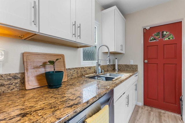 kitchen with dishwasher, light wood-type flooring, light stone counters, white cabinetry, and a sink