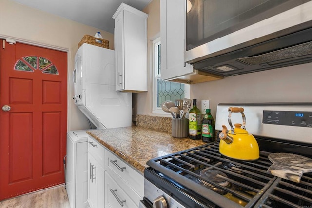 kitchen with white cabinetry, stacked washing maching and dryer, light wood-style floors, and stainless steel appliances