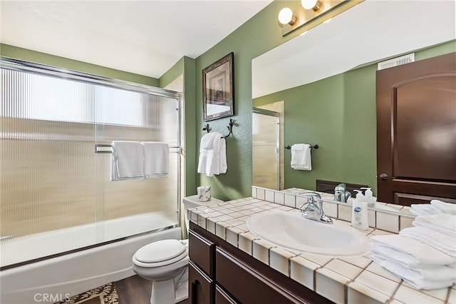 full bathroom with bath / shower combo with glass door, toilet, a textured wall, wood finished floors, and vanity