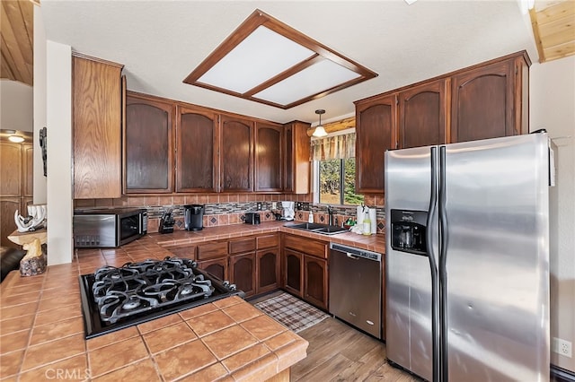 kitchen with decorative light fixtures, a sink, tasteful backsplash, tile countertops, and stainless steel appliances