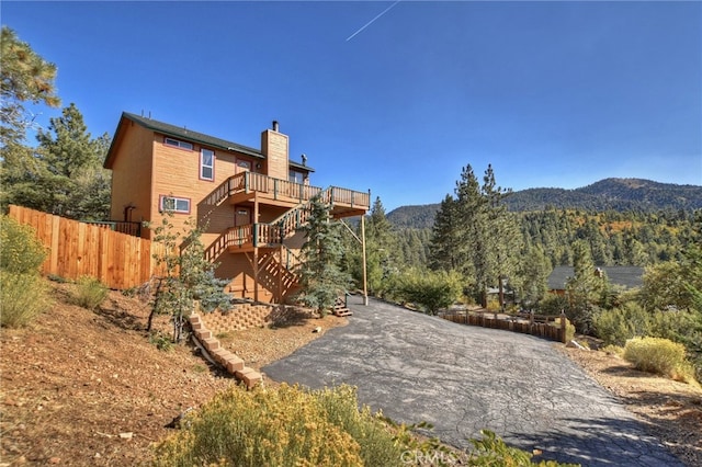 rear view of house featuring a deck with mountain view, aphalt driveway, stairs, fence, and a chimney