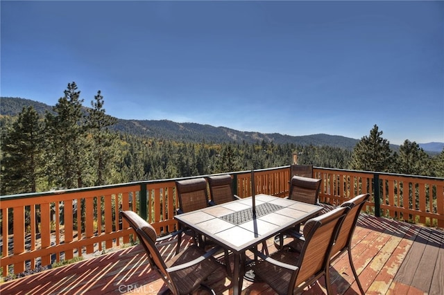 wooden terrace featuring a mountain view, outdoor dining area, and a wooded view