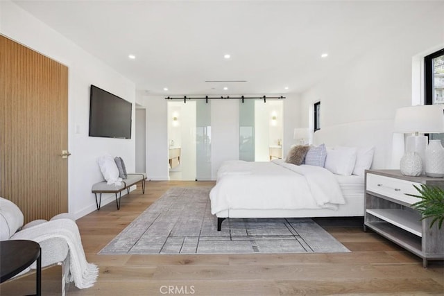 bedroom with wood finished floors, baseboards, recessed lighting, a barn door, and connected bathroom