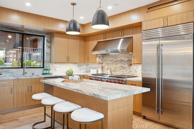 kitchen featuring light stone counters, a kitchen island, a sink, under cabinet range hood, and appliances with stainless steel finishes