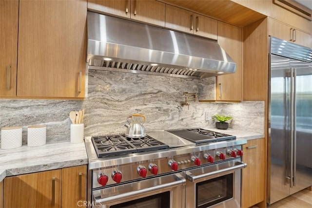 kitchen featuring under cabinet range hood, light stone countertops, tasteful backsplash, and high end appliances