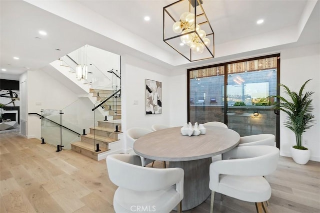 dining area with a notable chandelier, recessed lighting, light wood-style floors, a raised ceiling, and stairs