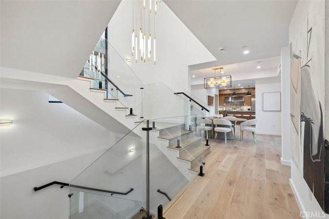 stairs featuring an inviting chandelier, recessed lighting, wood finished floors, and a towering ceiling