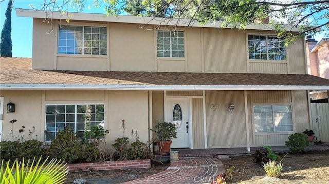 view of front of house featuring stucco siding, covered porch, and a shingled roof